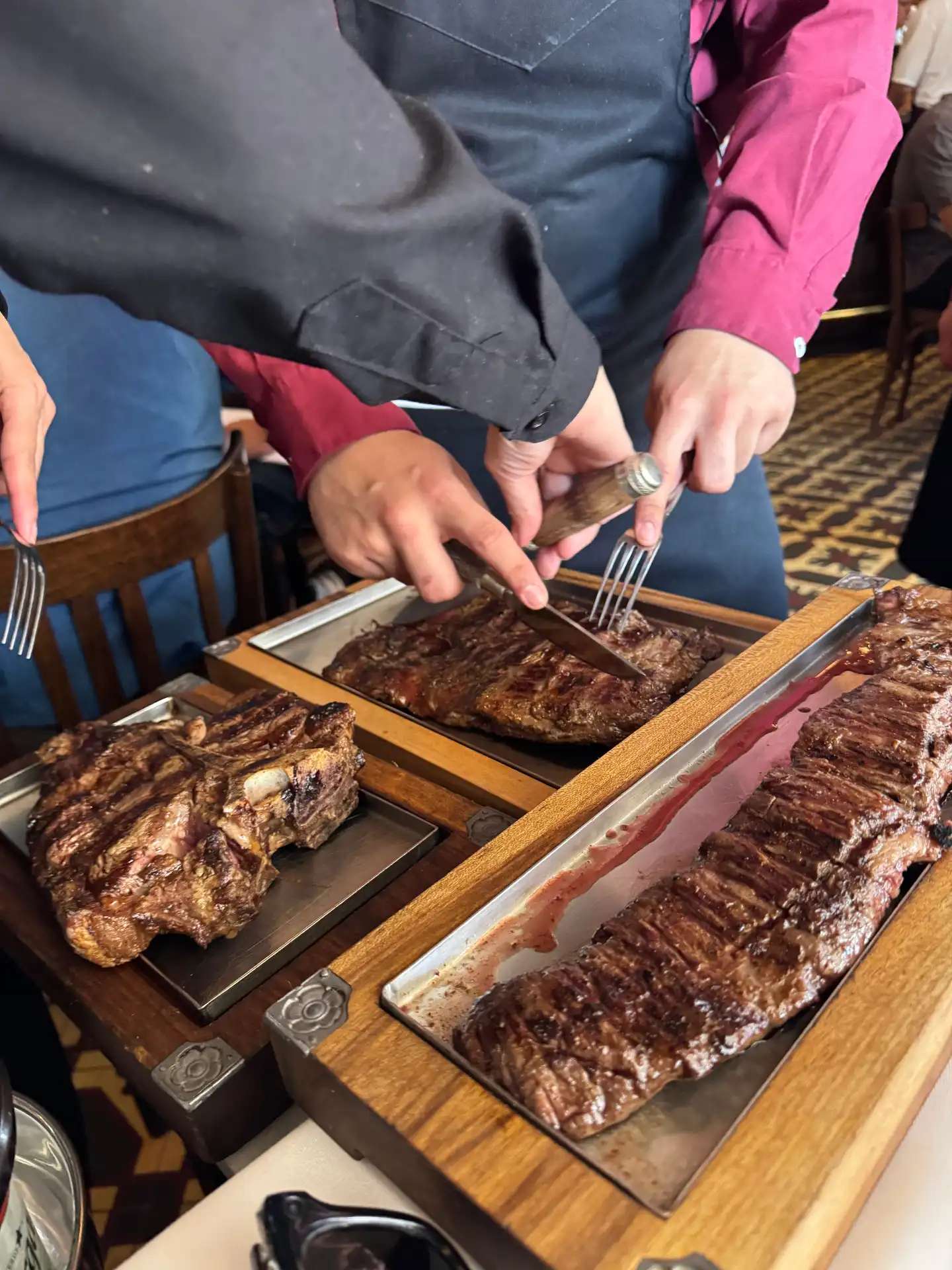 Waiter carving Argentine steaks tableside on wooden boards at a Mendoza parrilla