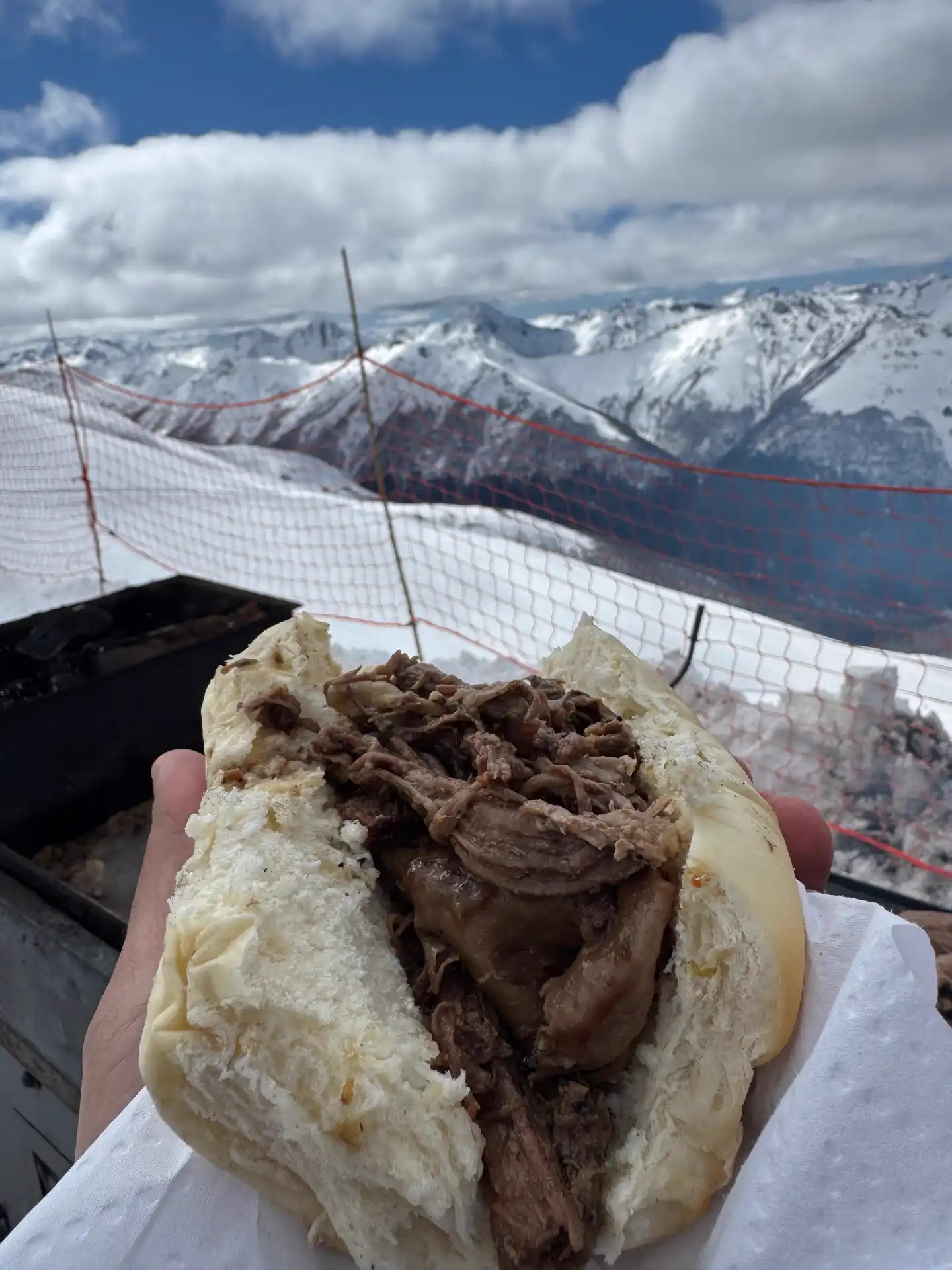 Argentine choripán sandwich held up against the snowy Andes at the top of Cerro Bayo
