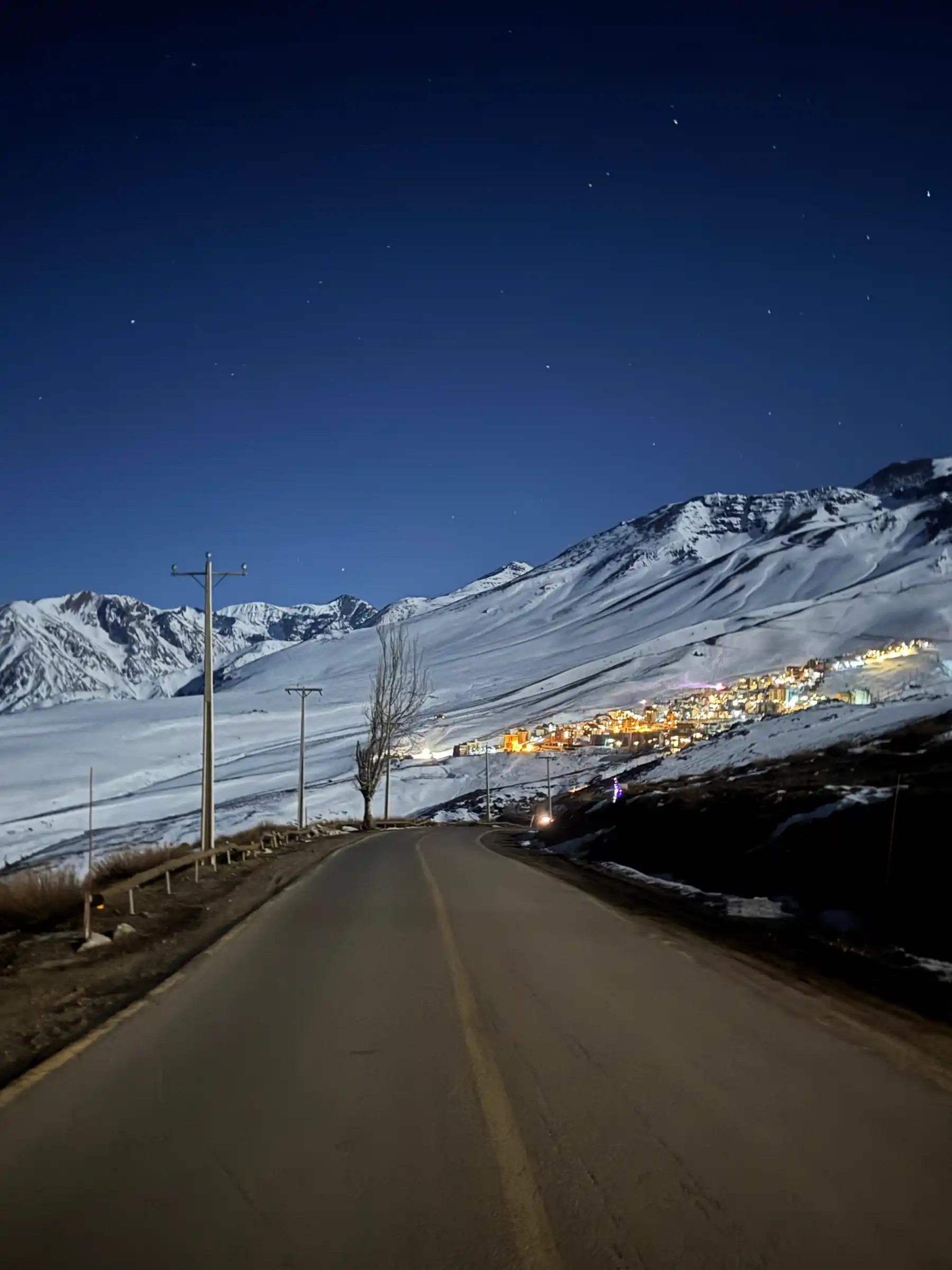 Night drive toward La Parva with lit village and snowy ridges under a starry sky
