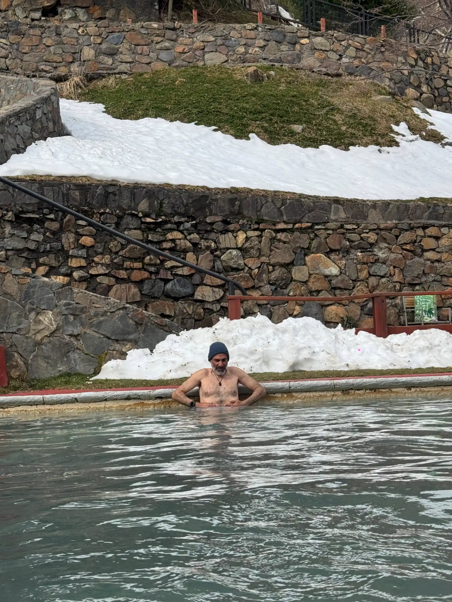 Outdoor thermal hot-spring pool at Nevados de Chillán base with snowbanks and stone retaining walls