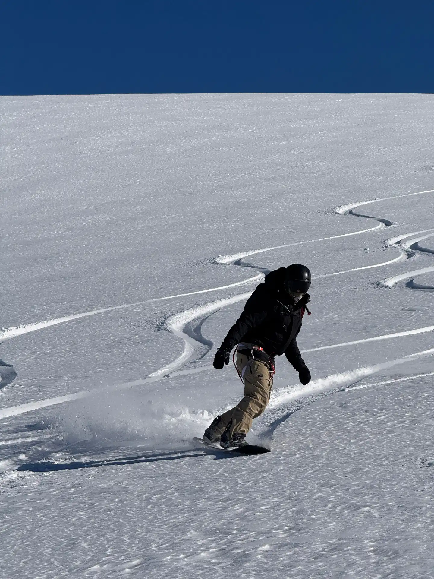 Snowboarder carving fresh tracks under a deep blue Las Leñas sky