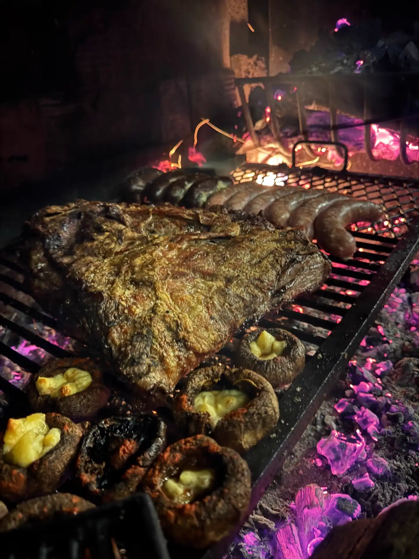 Patagonian asado cooking over open coals with sausages and mushrooms