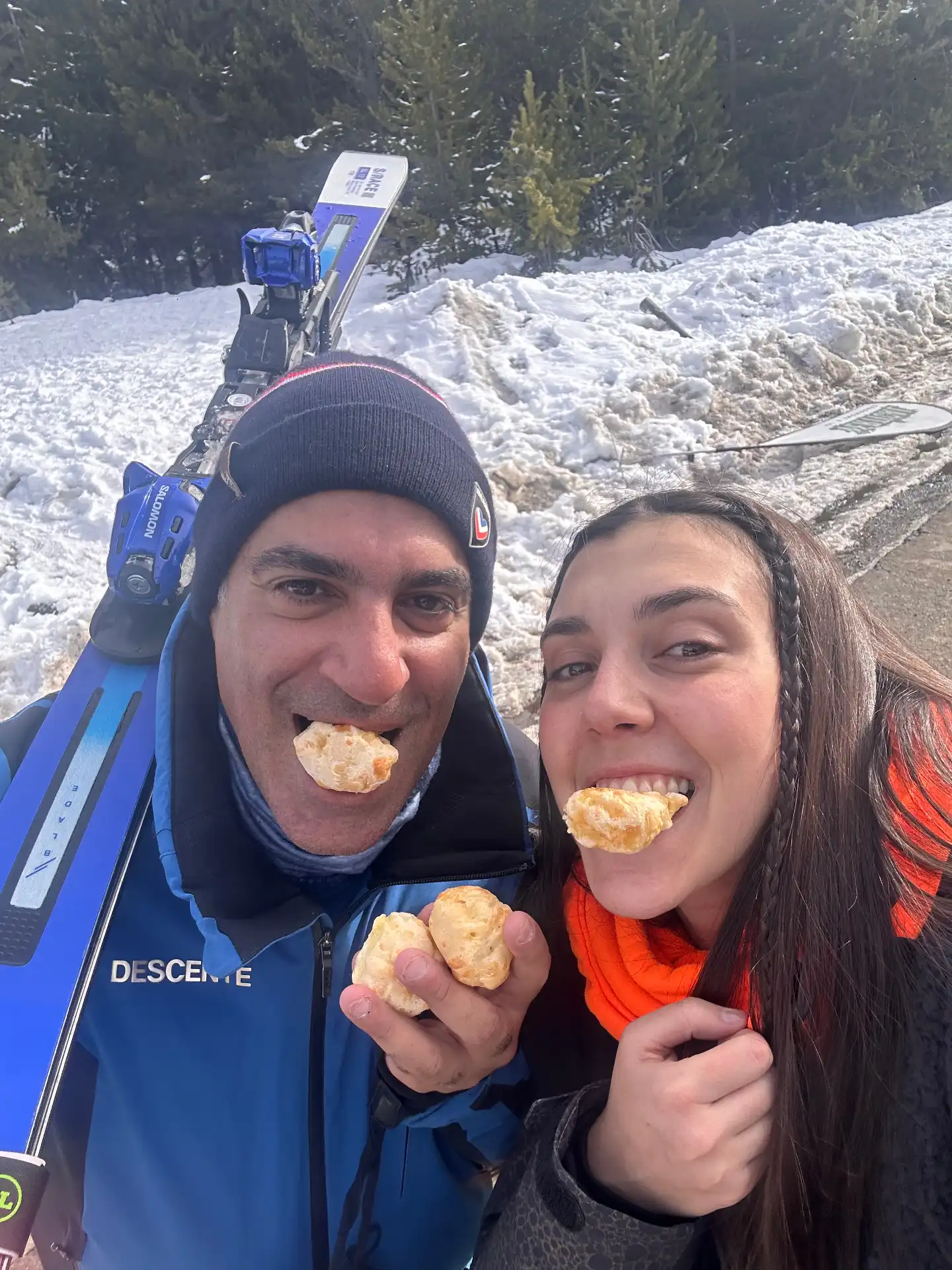 Couple eating warm pão de queijo beside skis in the snow during an Argentina ski trip