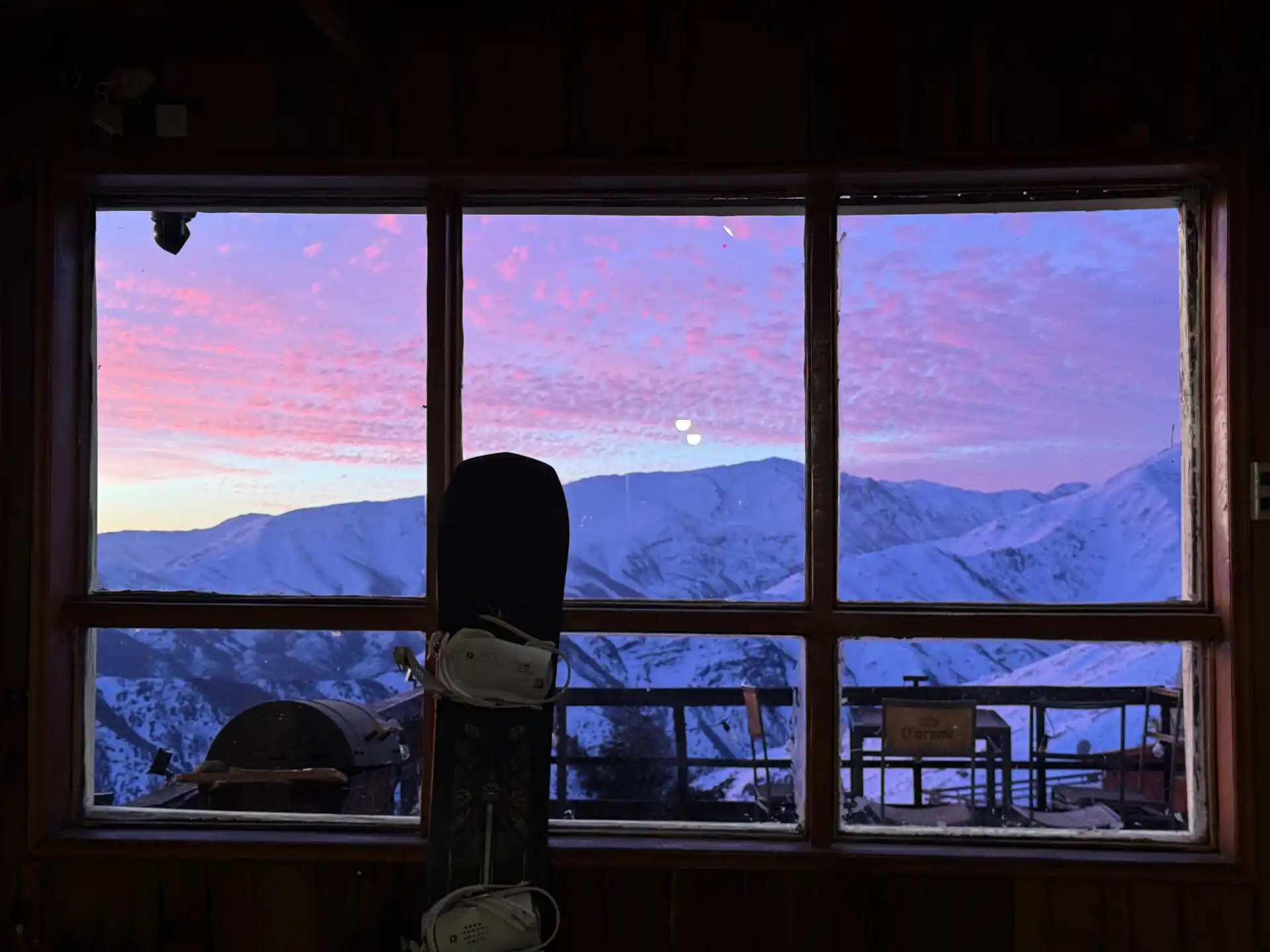 Snowboard silhouetted against a lodge window at sunrise over the Andes